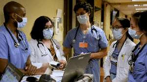 five people with PPE and stethoscopes talking in a hallway