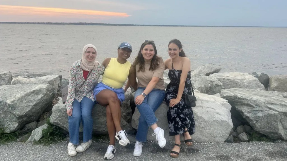 four people sitting on rocks along the ocean